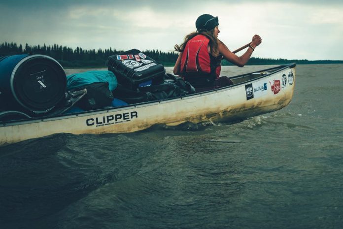 woman paddling a canoe loaded with camping gear