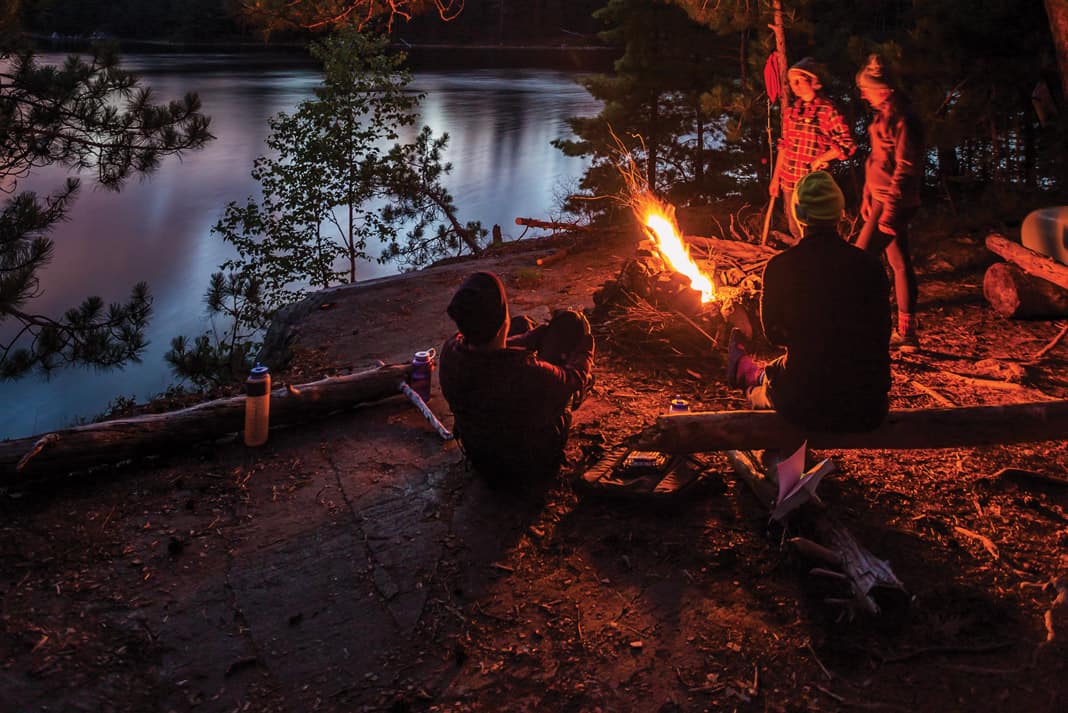 4 people standing by a fire at their canoe trip campsite