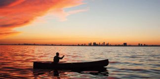 person paddling a canoe on calm waters during sunset with Toronto, Ontario in the background