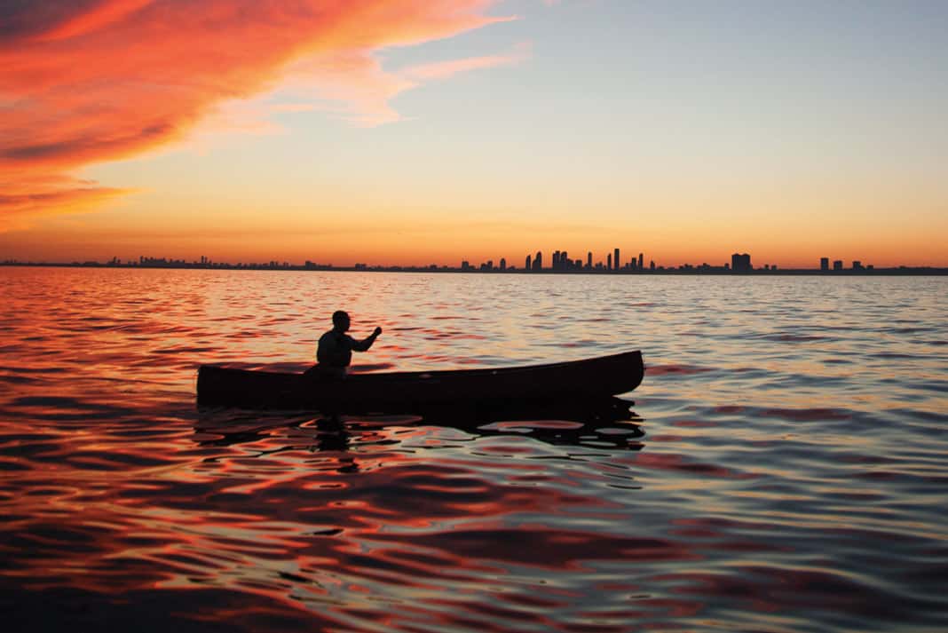person paddling a canoe on calm waters during sunset with Toronto, Ontario in the background
