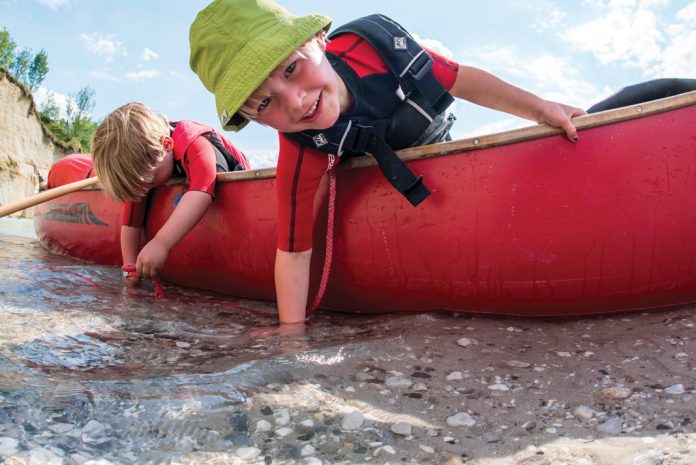 two kids in a canoe that has been beached playing with the water underneath them
