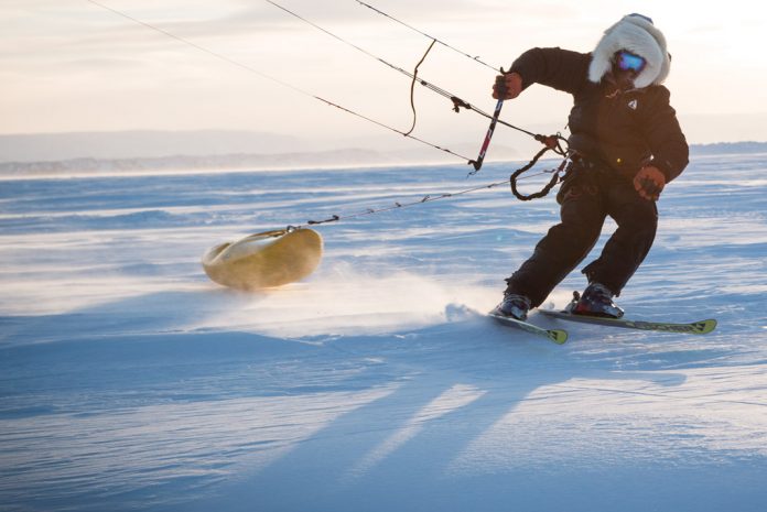 person dragging a kayak behind him while kitskiing on ground covered in snow and ice