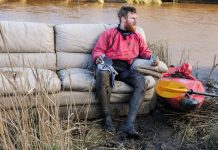 Beau Miles sitting on a couch next to his kayak and his kayak gear