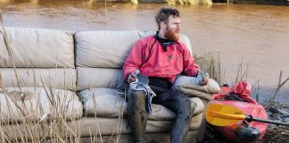Beau Miles sitting on a couch next to his kayak and his kayak gear