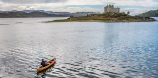 a person paddling a canoe on a lake towards a castle in Scotland, UK.