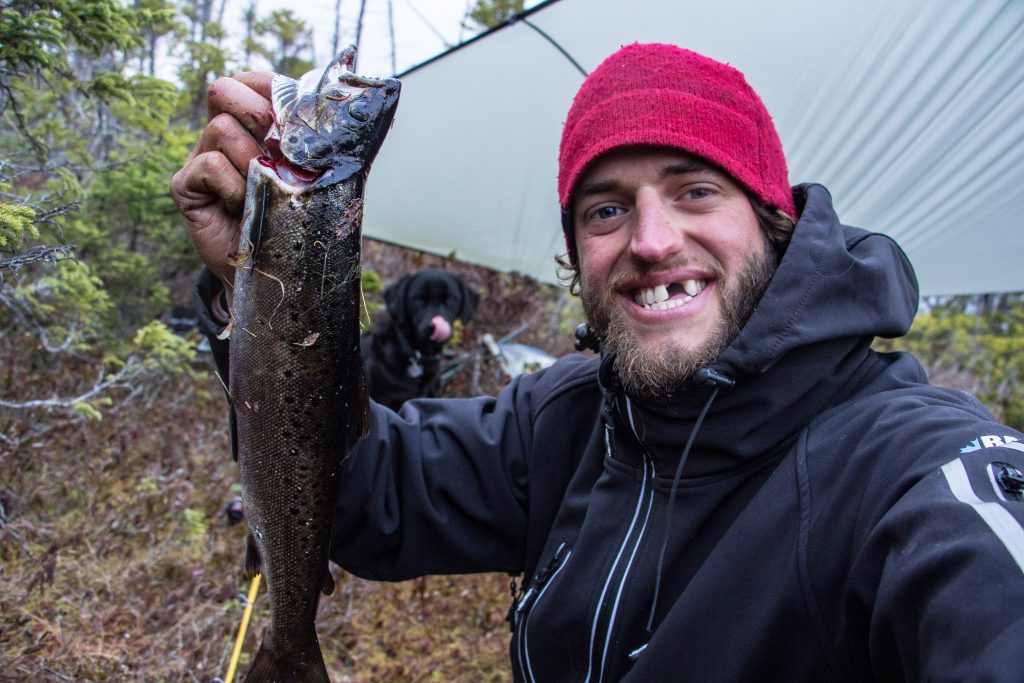 Justin Barbour holds large trout with his dog Saku in the background
