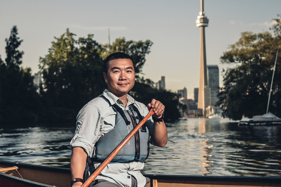 Michael Zhang canoe's on Lake Ontario with the CN Tower in Toronto, Ontario in the background