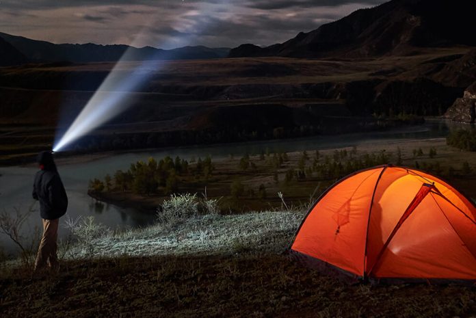 Camper standing next to tent with hat that has LED lights built into it