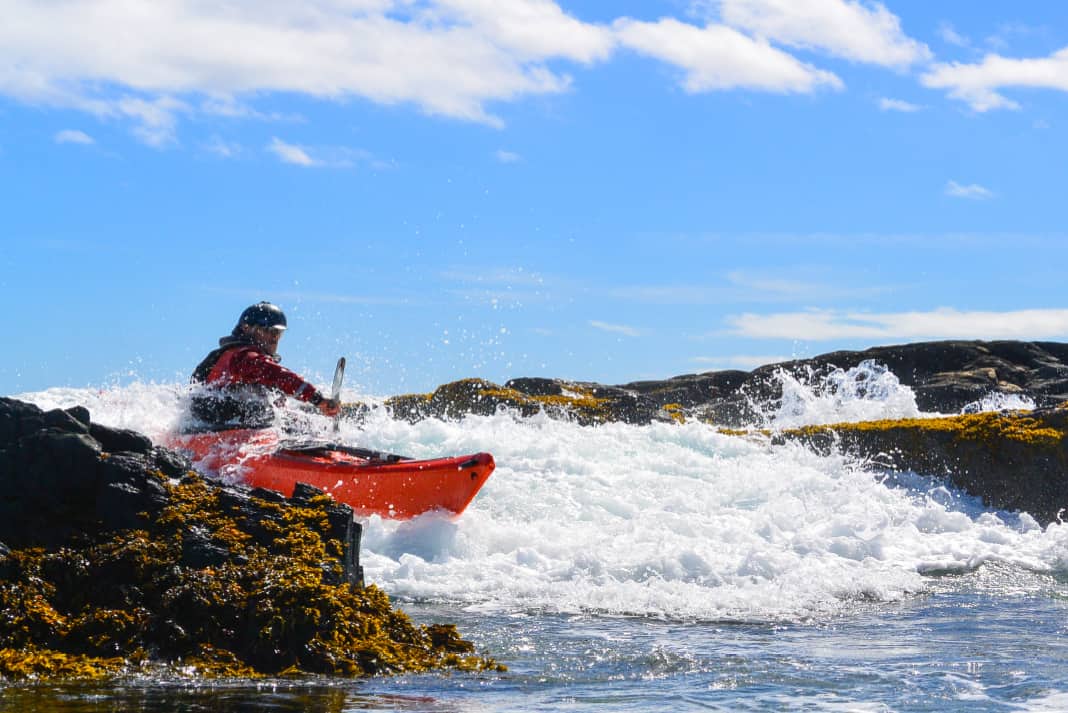 A sea kayaker bounces off a rock in a plastic kayak