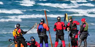 A group of expedition kayakers stand on a beach wearing Gore Tex outdoor gear
