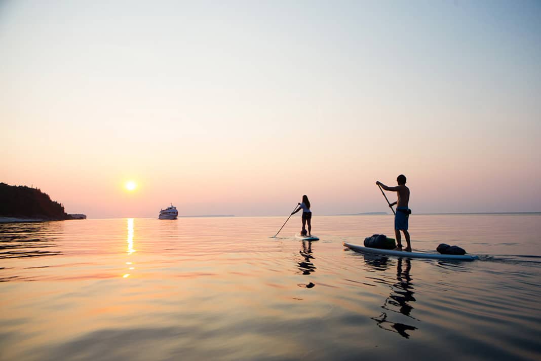Paddleboarders paddling into sunset