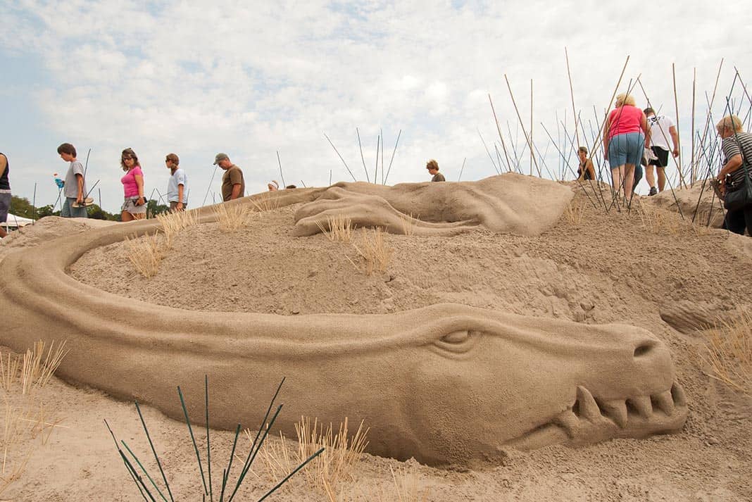 Alligator made in the sand with people walking in background