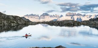 Person paddling a kayak across a lake with mountains in background