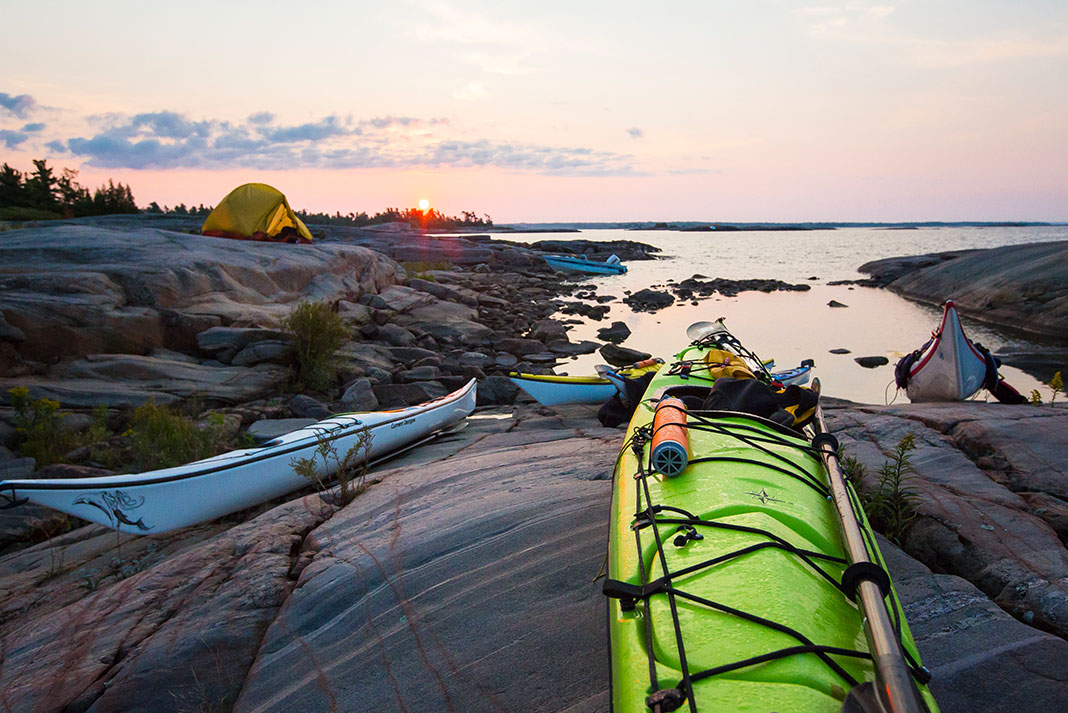 Sea kayaks pulled up on rocks with tents in background