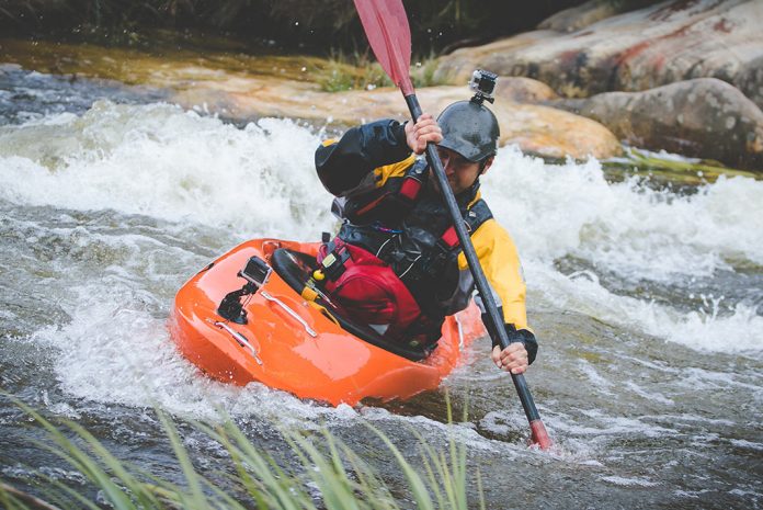 Man in orange whitewater kayak with yellow and black drysuit