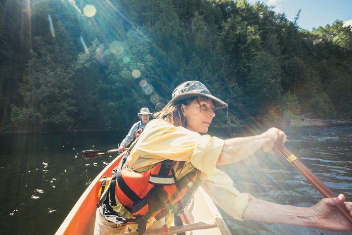 Woman and man wearing hats and long-sleeve shirts in a canoe with sun flare