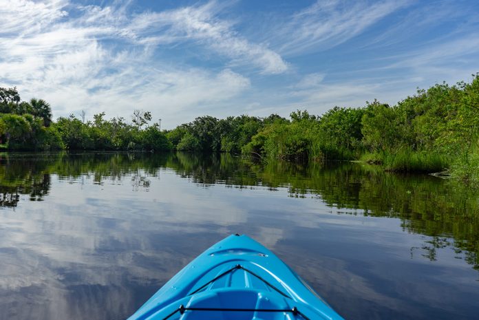 Front of a kayak looking out over calm lake lined with trees
