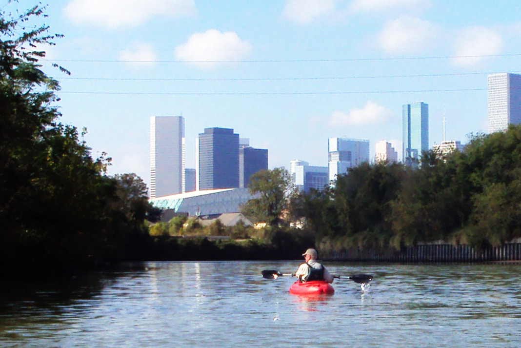 Man kayaking down river toward Houston skyline