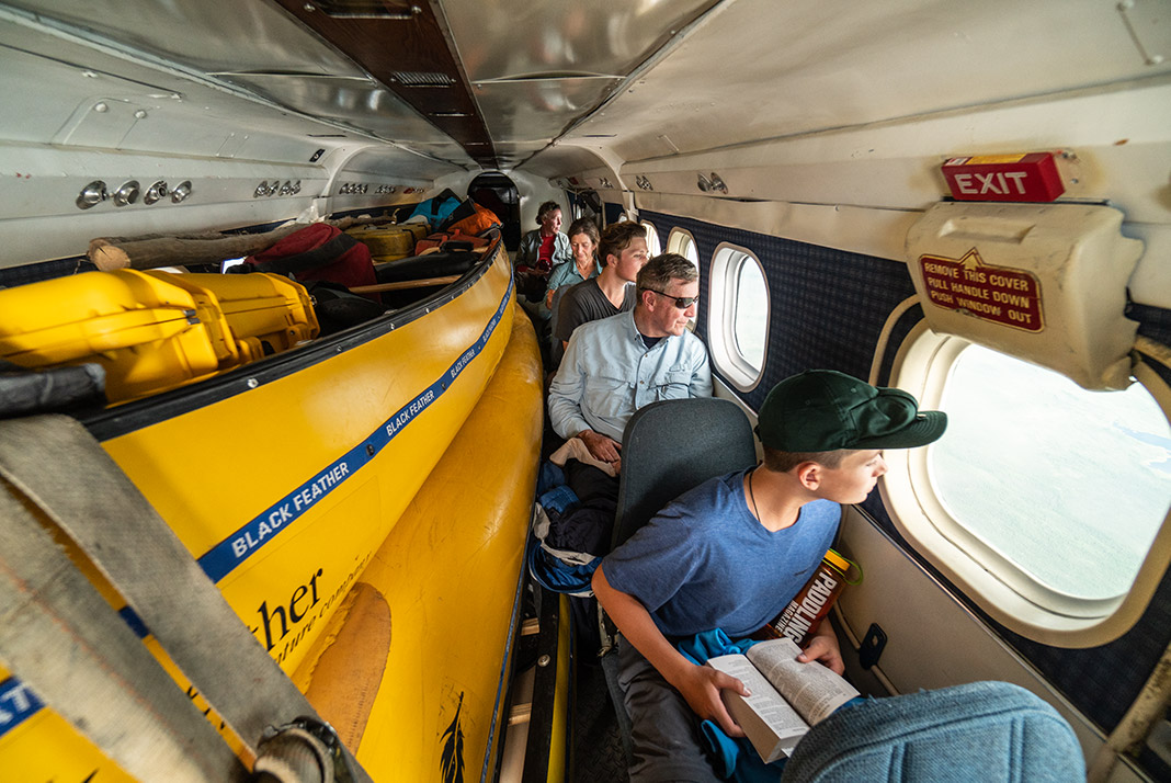People sitting in single seats on a plane with canoes in middle of aircraft.