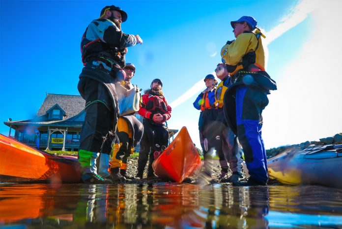 Paddlers standing facing each other with sea kayaks on the ground