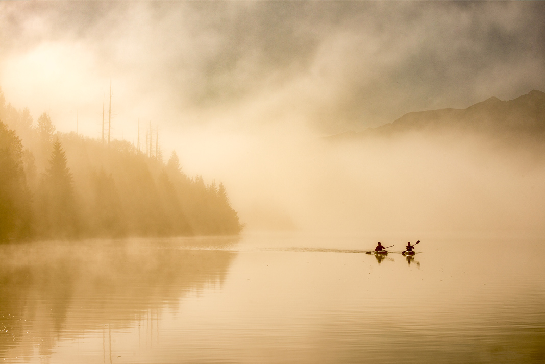 Two kayakers paddling along misty coast