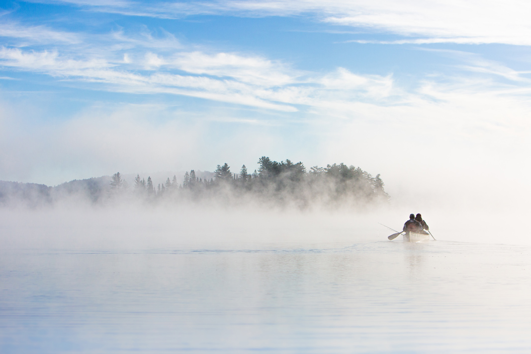 Two figures paddling a canoe on a foggy lake