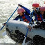 Guide To Whitewater Rafting: What To Expect, Where To Go, Safety & More People paddling hard in a raft