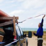 A Dirtbag’s Guide To Building A Canoe & Kayak Rack For Your Pickup Truck Man strapping down canoe on wooden rack on bed of pickup truck.