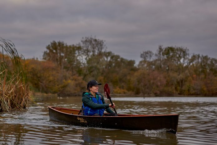 Woman solo paddling canoe with double blade paddle