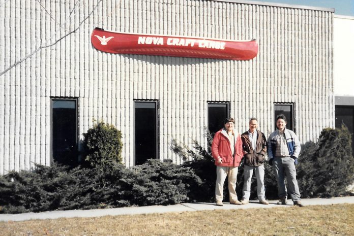 Three men standing outside building with canoe hanging above