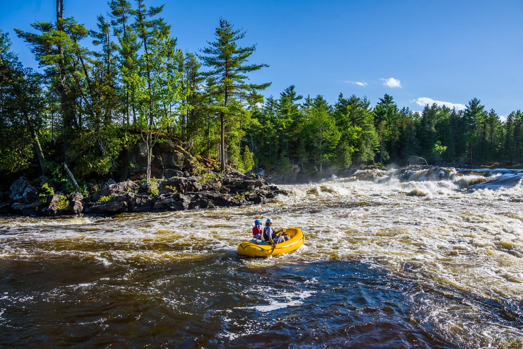 A father and son paddle a yellow raft down a river.