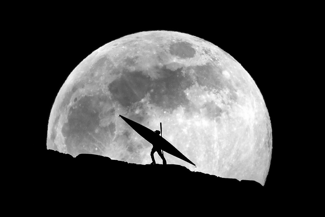A kayaker silhouetted against the full moon