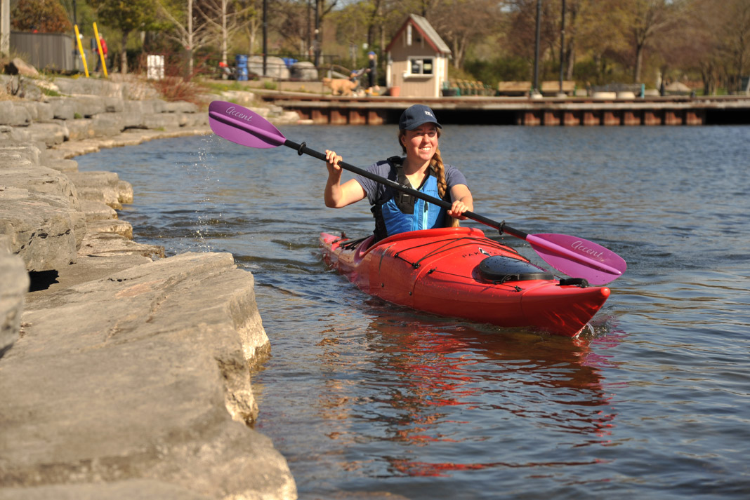 A woman paddles along the shore in a Pakayak Bluefin 14 packable kayak
