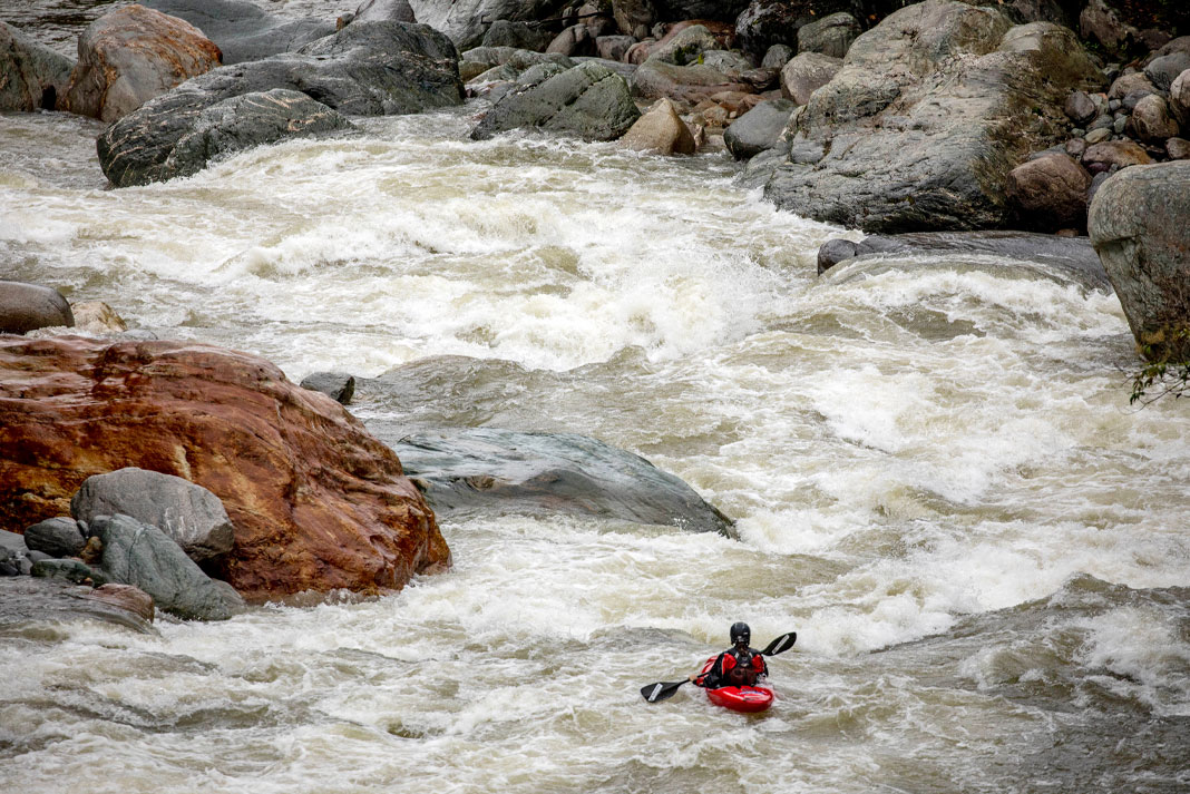 A woman paddles the amazon river in a red whitewater kayak