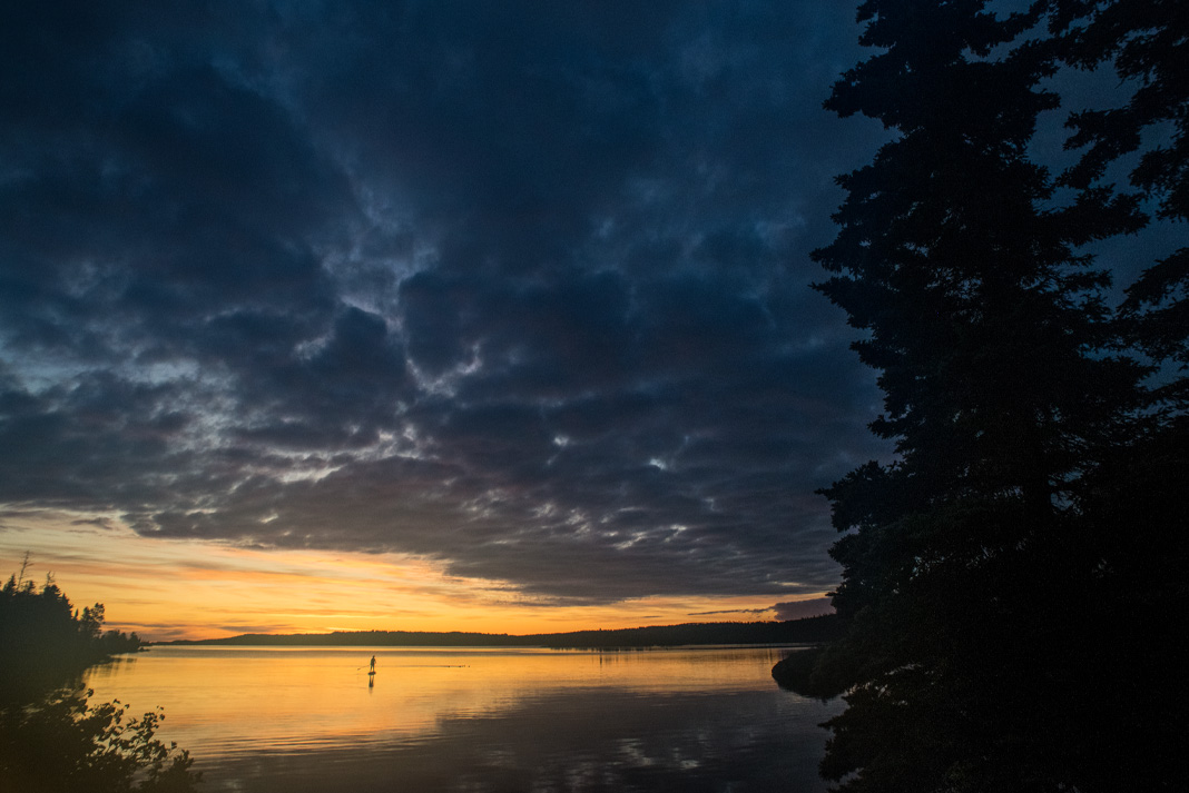A single paddleboards crosses Lake Superior at sunset