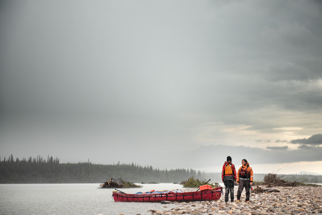 Two paddlers stand beside a lake with their canoe in the backcountry.