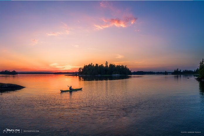 A kayaker paddles towards and island at sunset