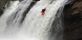 Kayaker running a waterfall with another kayaker waiting below.