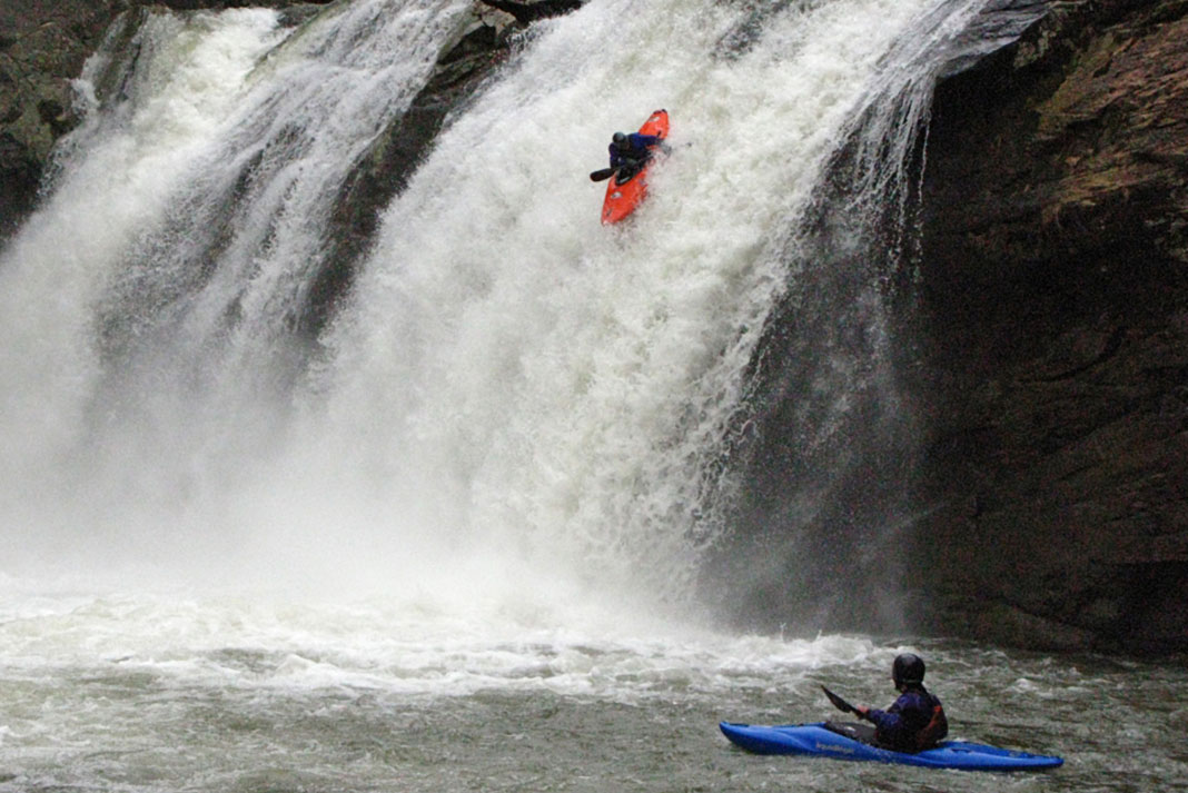 Kayaker running a waterfall with another kayaker waiting below.