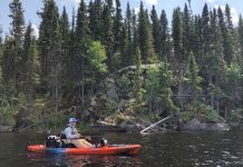 Kayak Angler paddles along rocky short for smallmouth bass