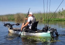 man paddles his kayak rigged for lake fishing