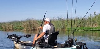 man paddles his kayak rigged for lake fishing