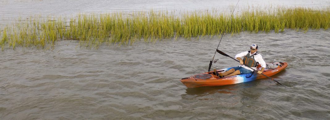 Man paddling an orange sit-on-top fishing kayak