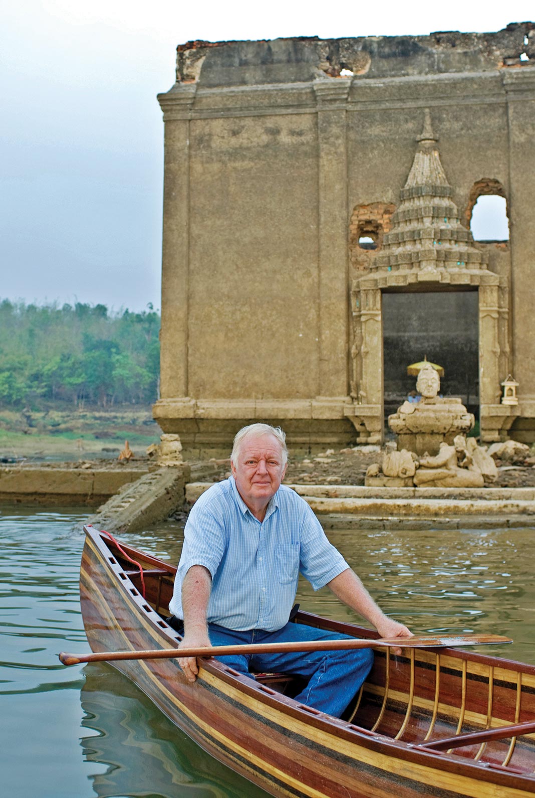 Man sitting in wooden canoe with Buddha in background