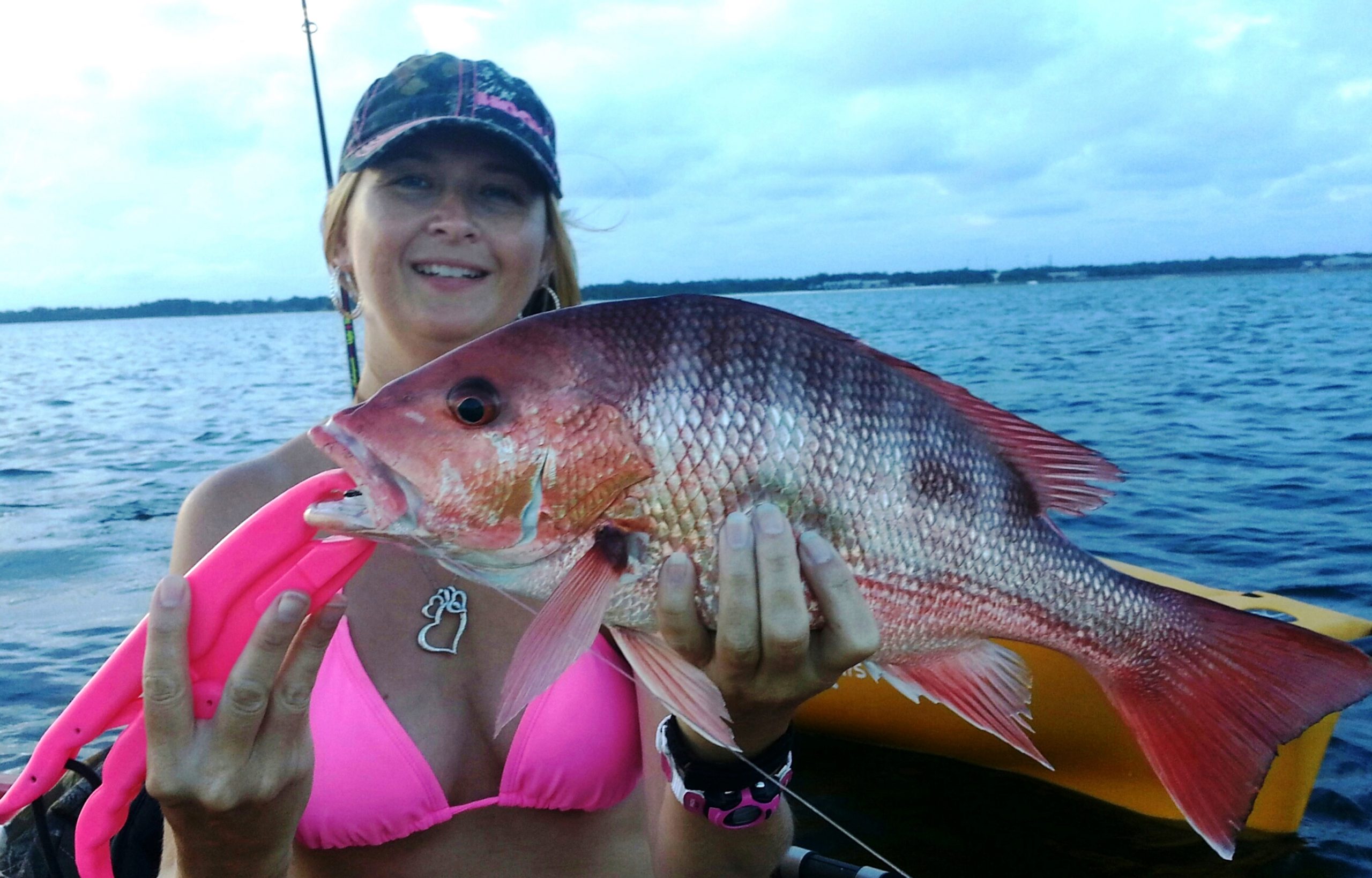 woman in fishing kayak holds red snapper up to camera