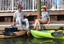 A couple has drinks on the dock by their fishing kayaks