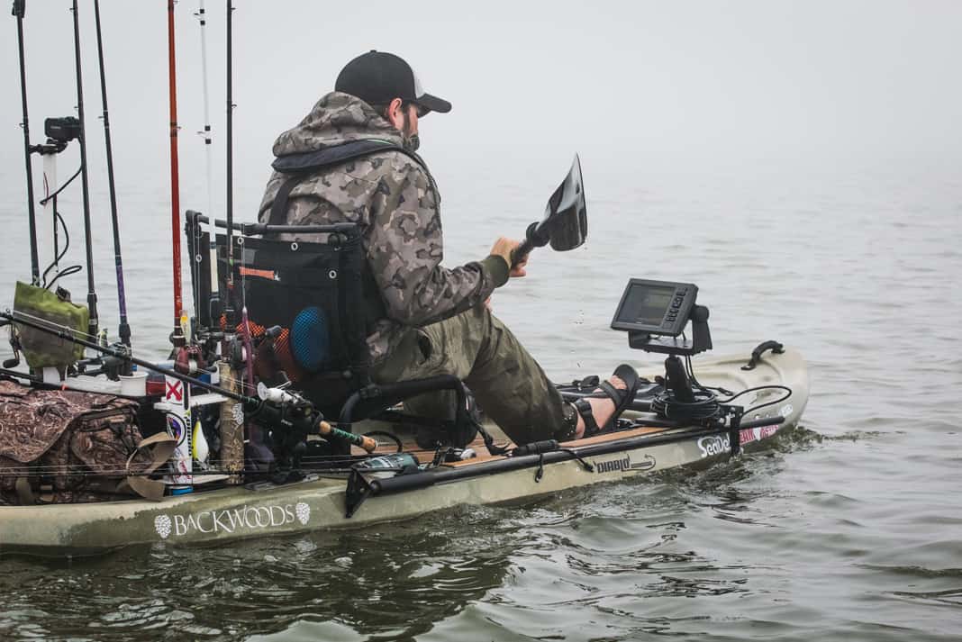 man paddles a fishing kayak with the best fish finder