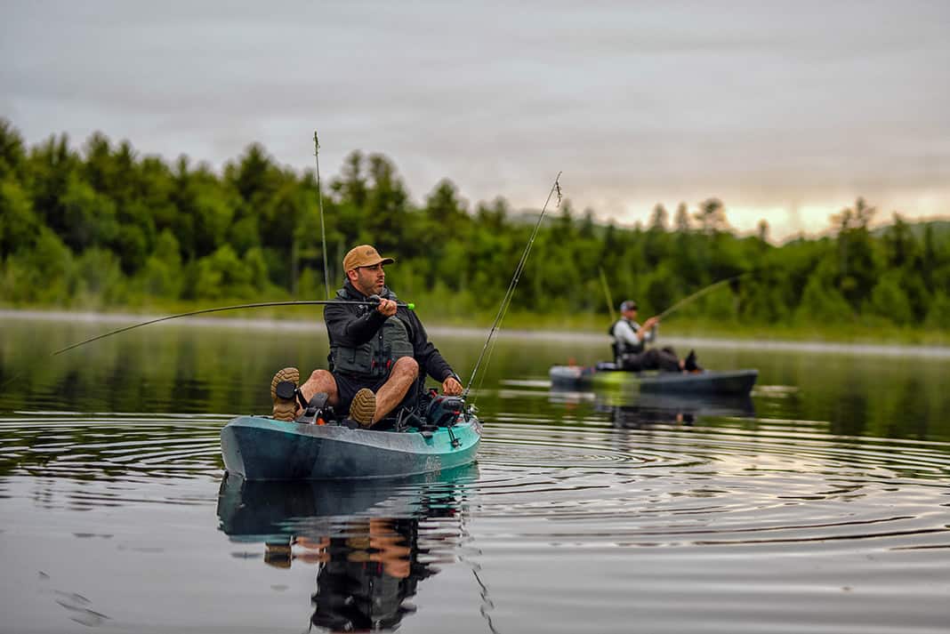 Two people casting while sitting on fishing kayaks