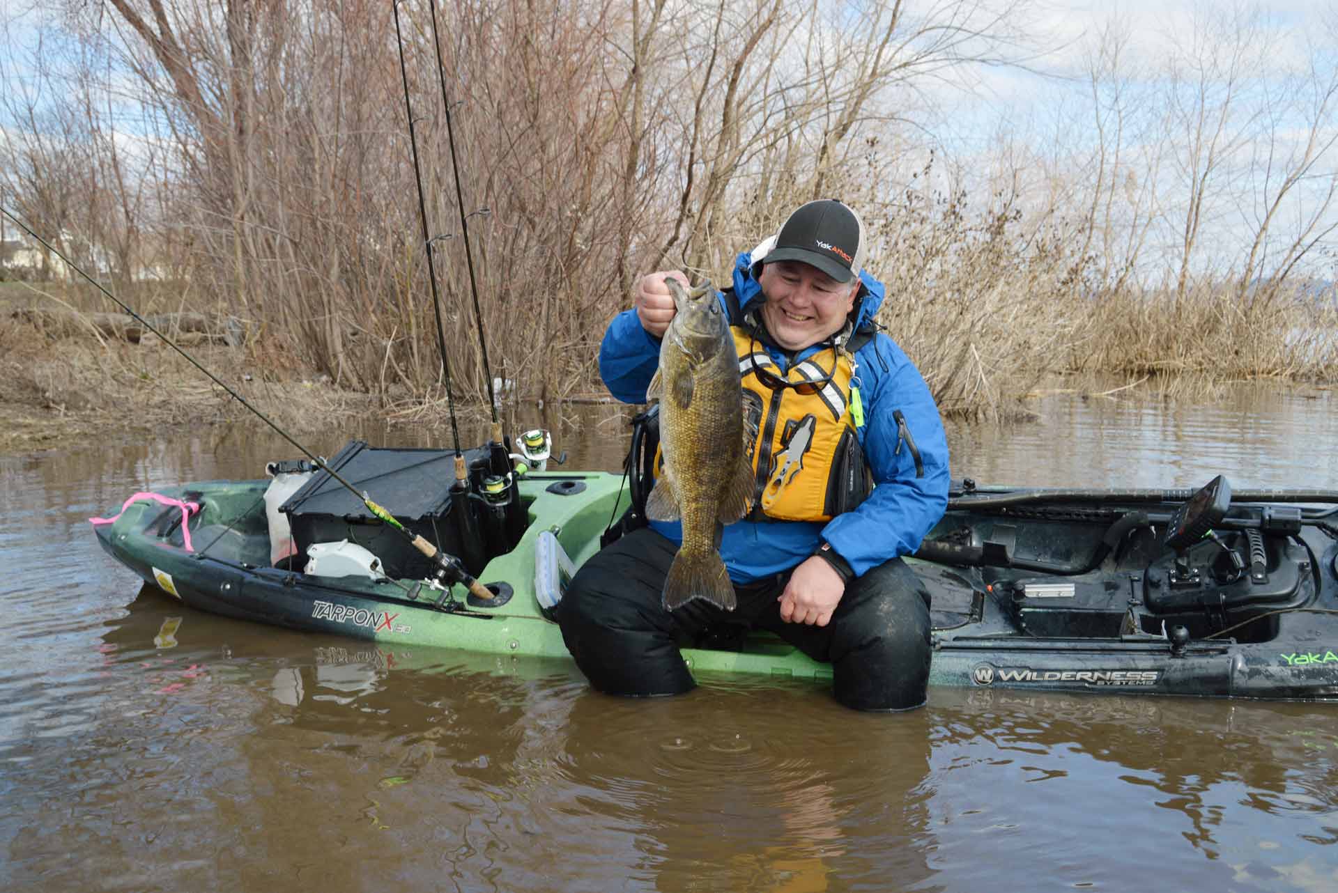 Angler holding up bass on side of kayak