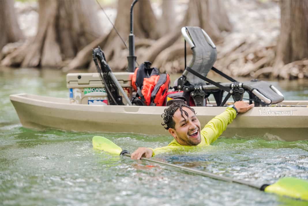 man swims alongside his fishing kayak after flipping it